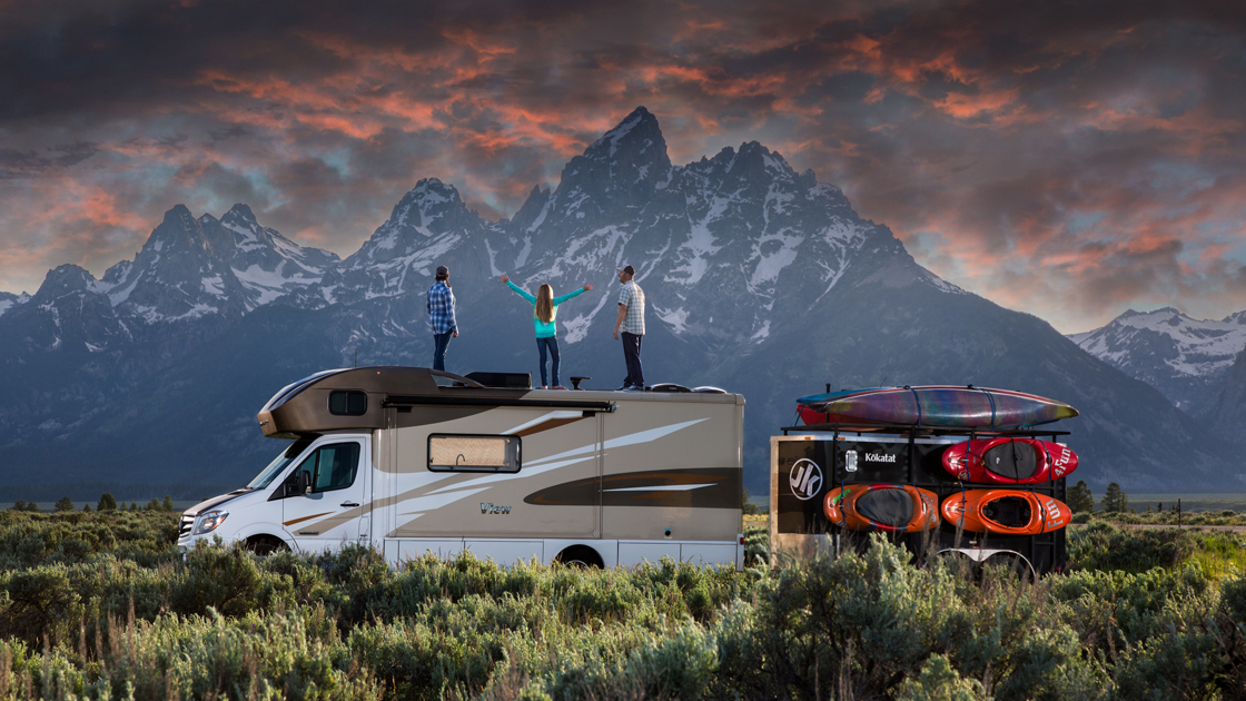 Three people standing on RV in front of Mountain
