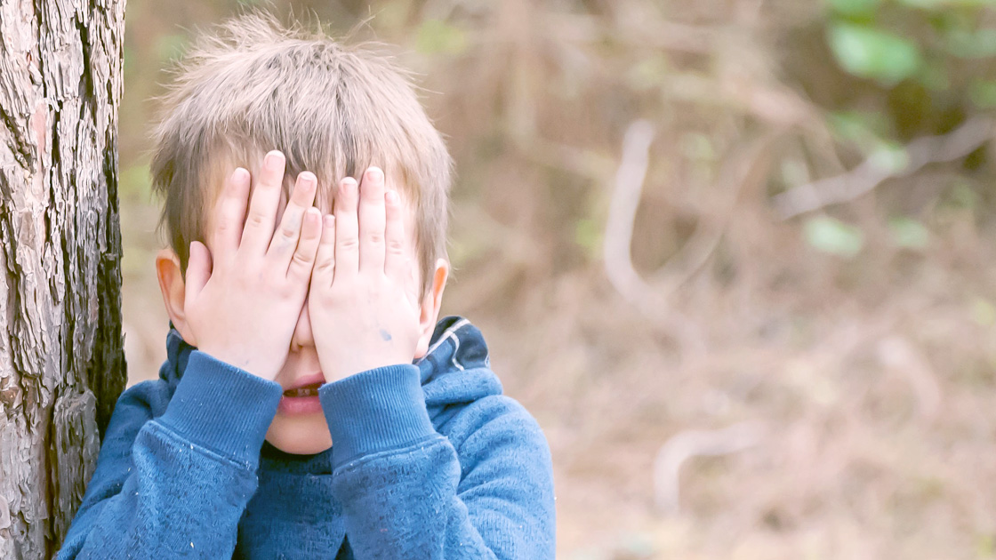 Boy covering his face near a tree outside