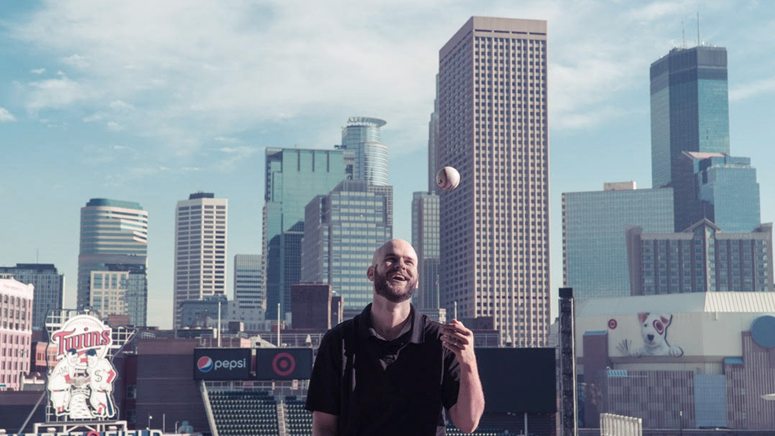 Man throwing baseball in the air with skyline behind them