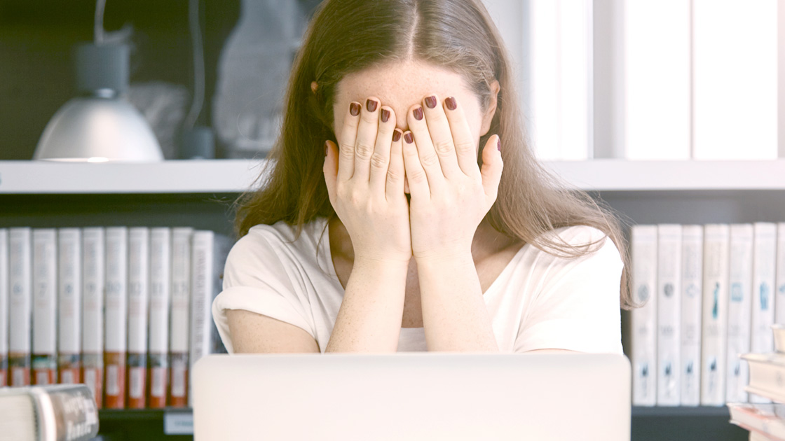 Woman holding hands over her face in front of a computer