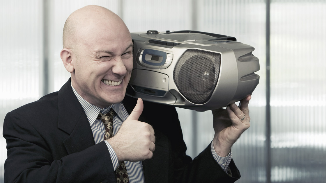 Bald businessman giving a thumbs up sign while listening to a boombox radio on his shoulder