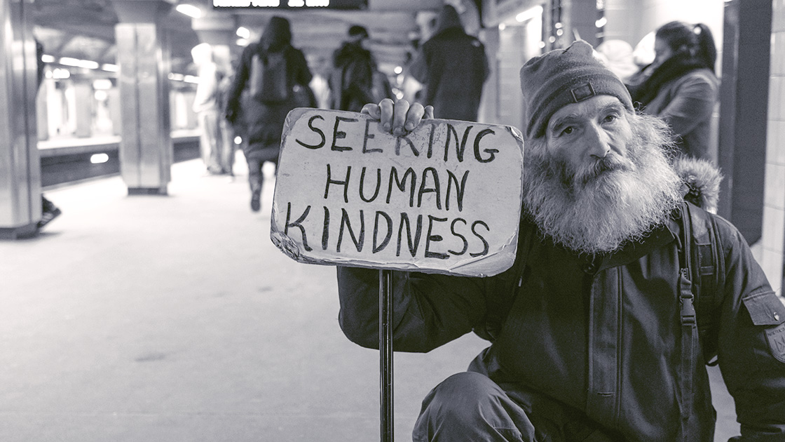 Photo of old man in subway holding sign that says, "Seeing Human Kindness"