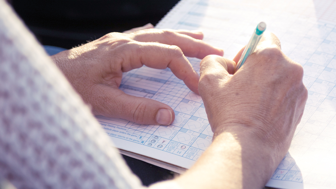 Person filling out baseball scorecards with a pencil