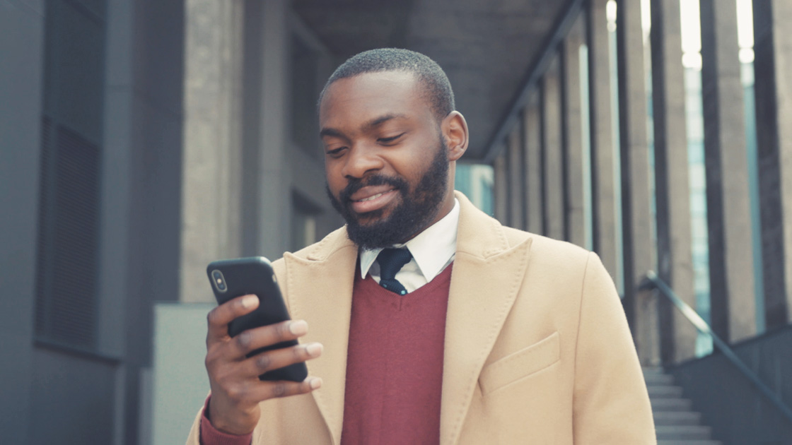 Business man in a metropolitan setting smiling while looking down at his smartphone
