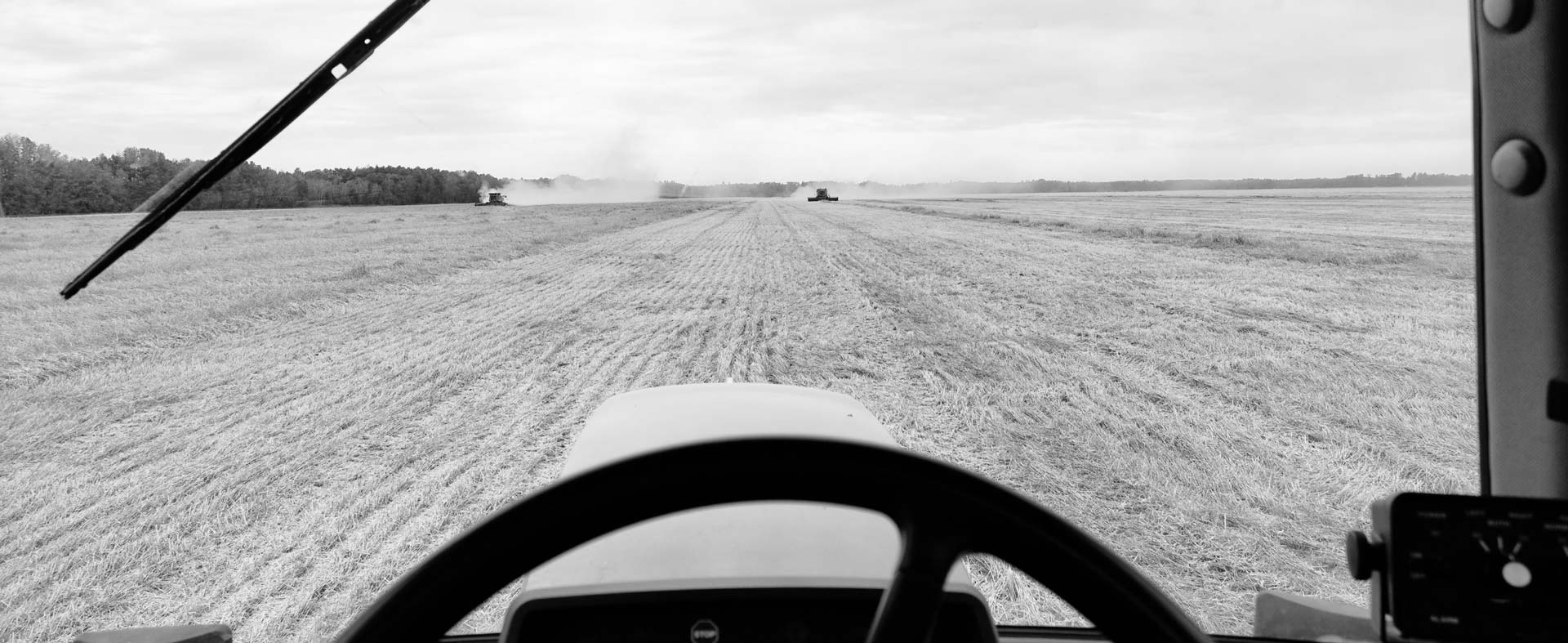 View front the driver's seat of a combine out into a field; Grayscale photo