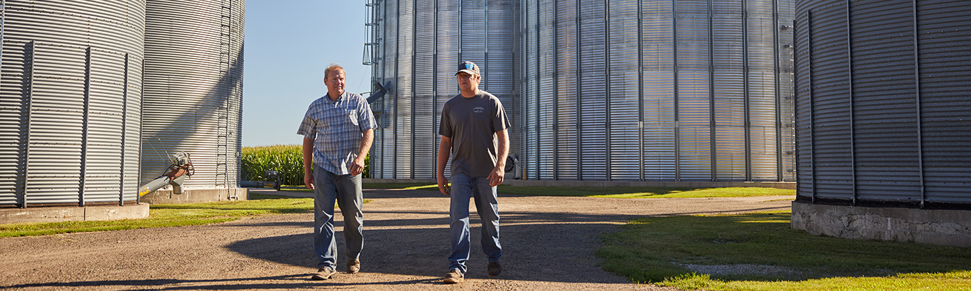 two farmers walking between grain silos on a sunny day