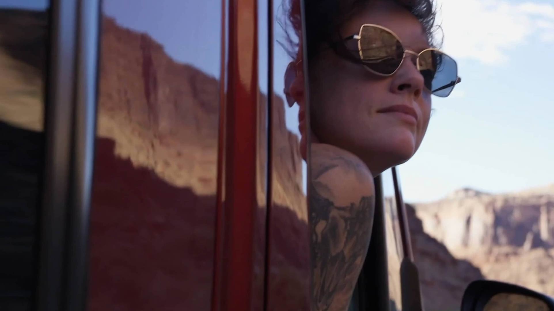 Woman wearing sunglasses looks out the window of her motorhome at the horizon