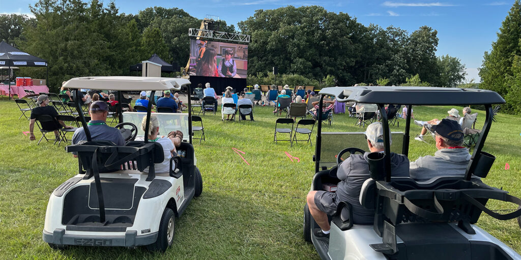 people sitting in golf carts watching a movie on a lawn