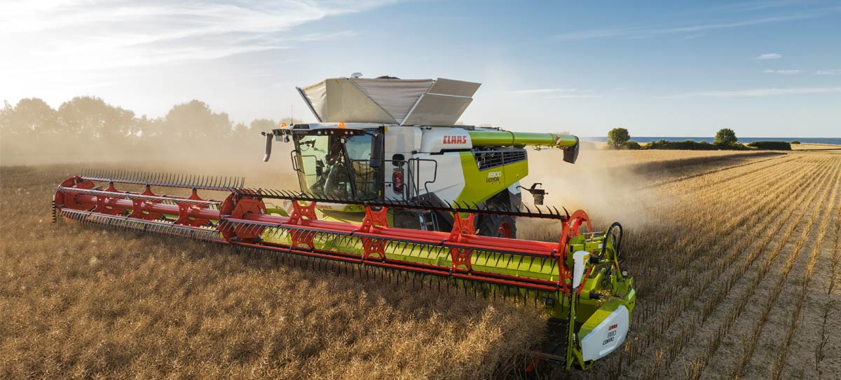 CLAAS combine harvesting wheat with a sunrise in the background